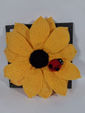 Large yellow crochet sunflower with a detachable red ladybird in a dark wooden frame