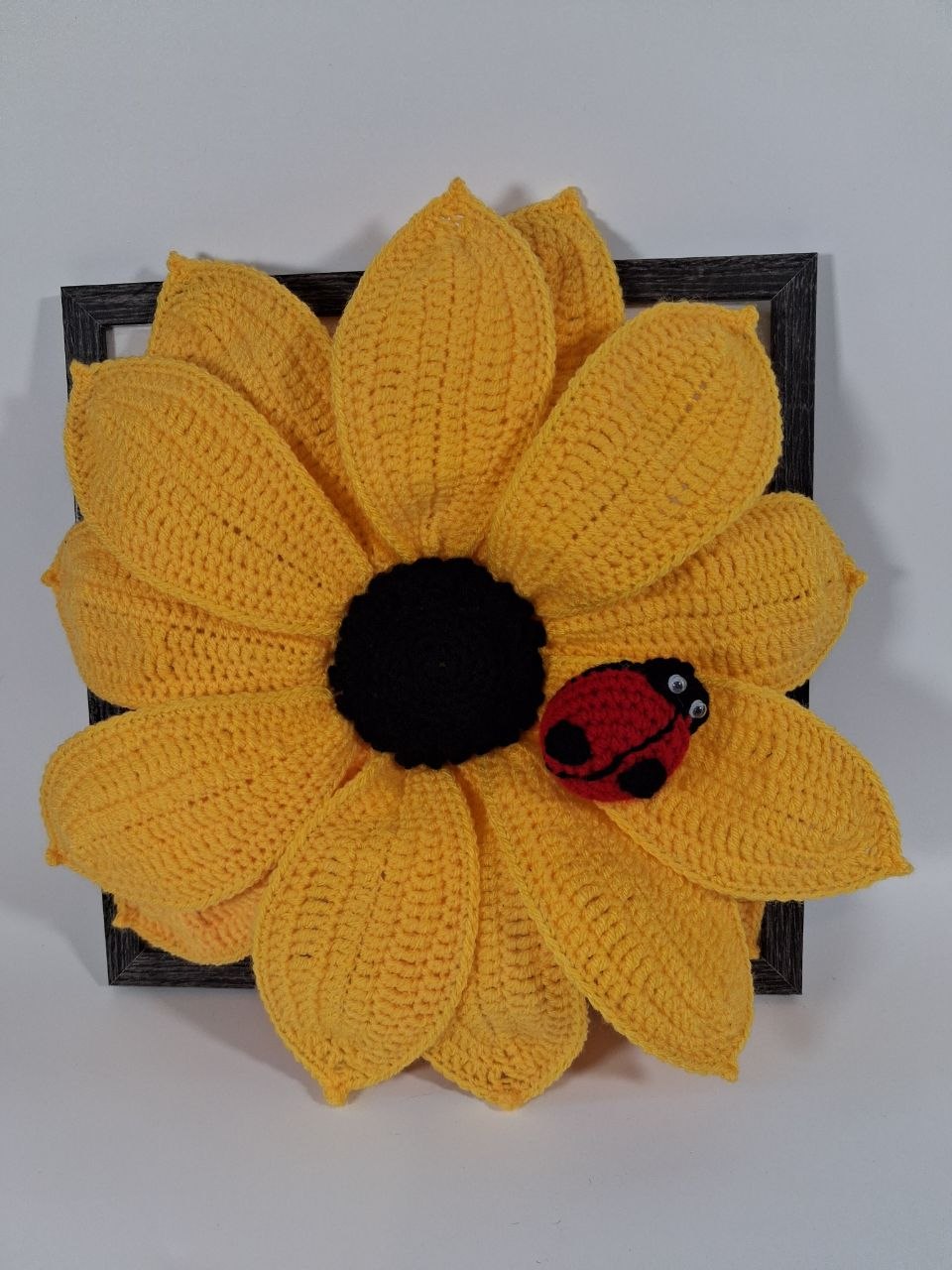 Large yellow crochet sunflower with a detachable red ladybird in a dark wooden frame