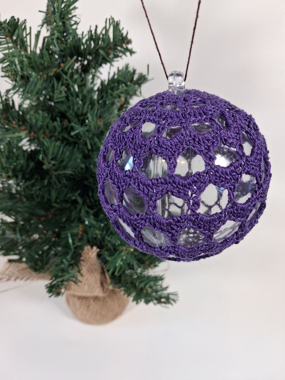 Handmade purple crochet cover on a clear hollow plastic Christmas bauble hanging from a tree