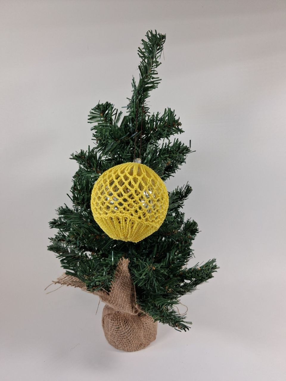 Handmade  crochet cover on a clear hollow plastic Christmas bauble hanging from a tree