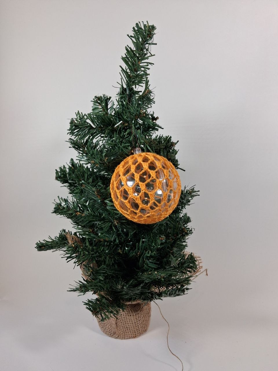 Handmade  crochet cover on a clear hollow plastic Christmas bauble hanging from a tree