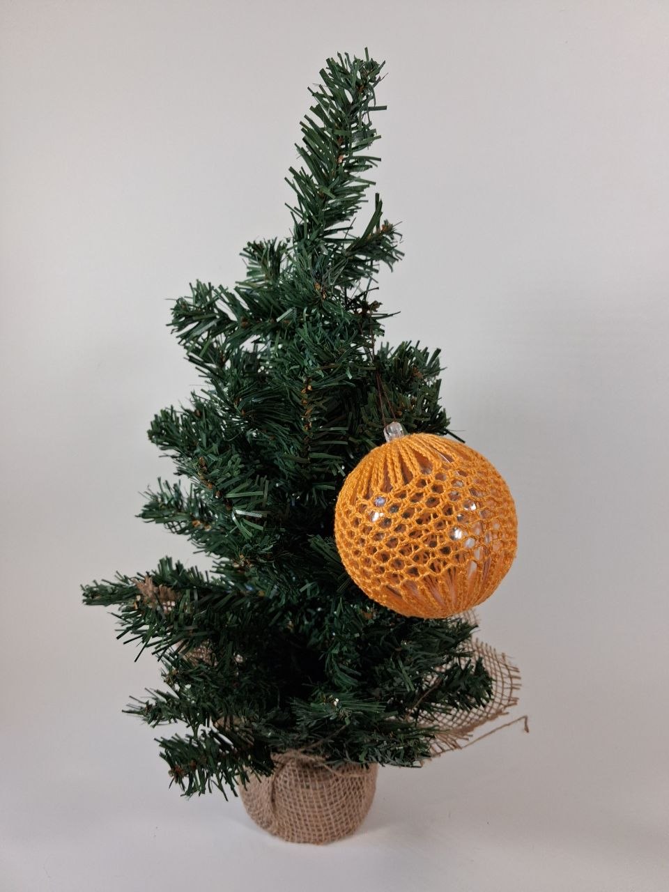 Handmade  crochet cover on a clear hollow plastic Christmas bauble hanging from a tree